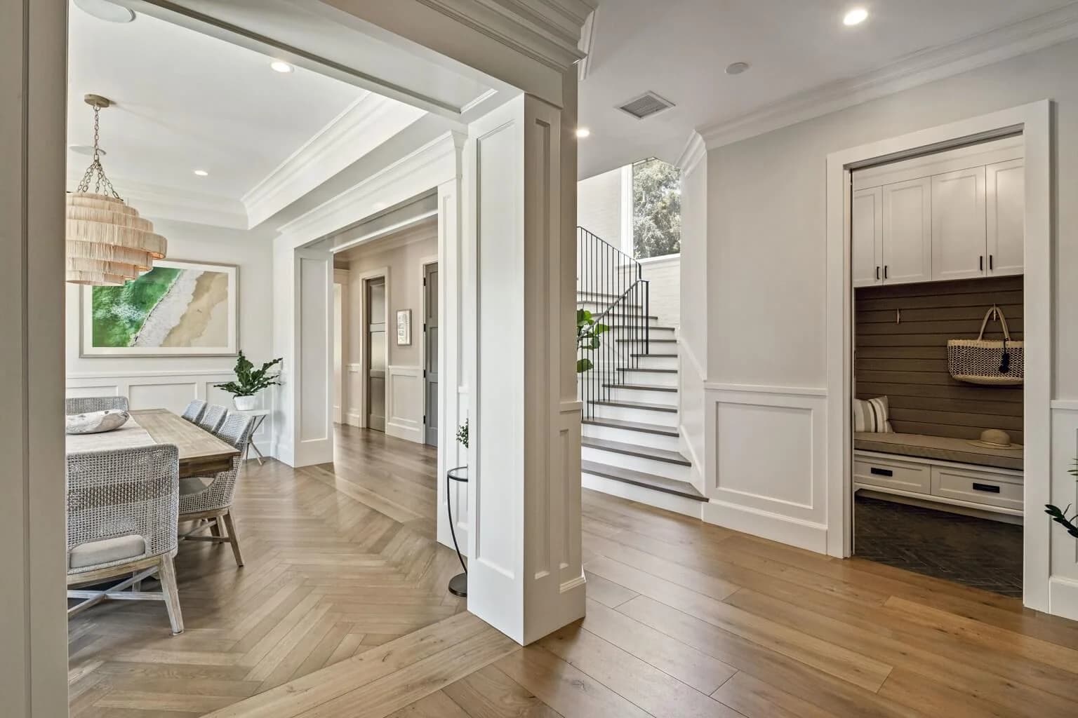 Entry hall with herringbone wood floors, staircase, dining room, and built-in mudroom bench