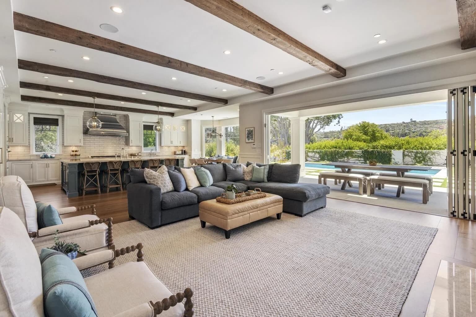 Open-concept great room with exposed beams flowing into the kitchen and out to the pool