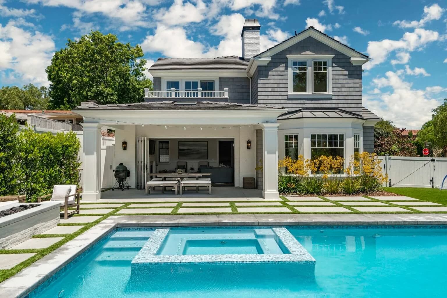 Rear exterior with covered patio and pool with raised spa under a blue sky