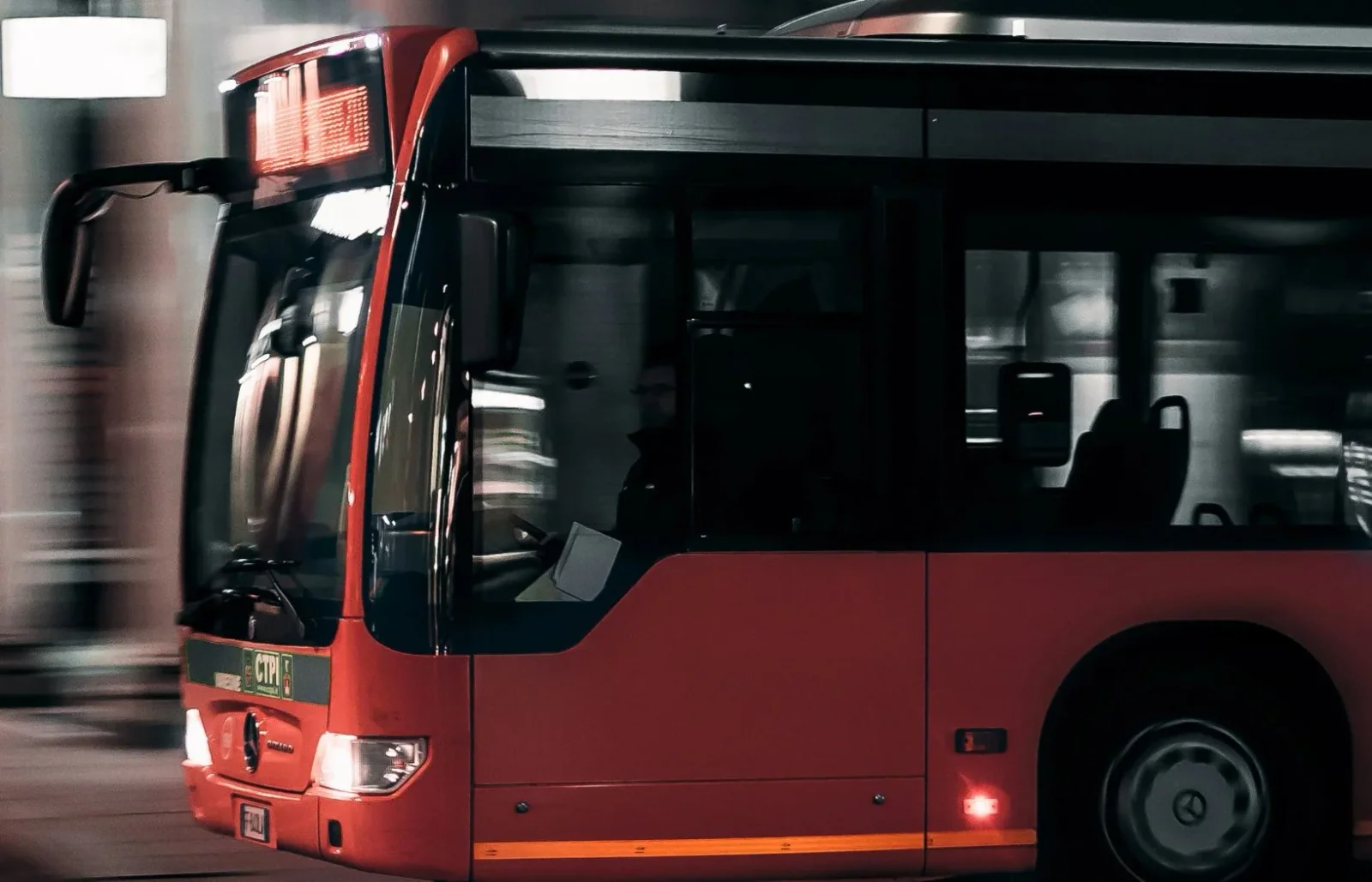 Red city transit bus pulling away from a station in low light