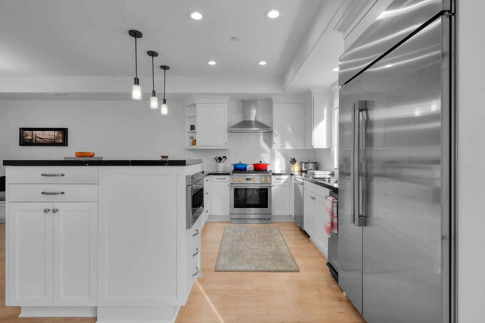 Remodeled white kitchen with stainless appliances, island, and hardwood floors by DECOMA Industries