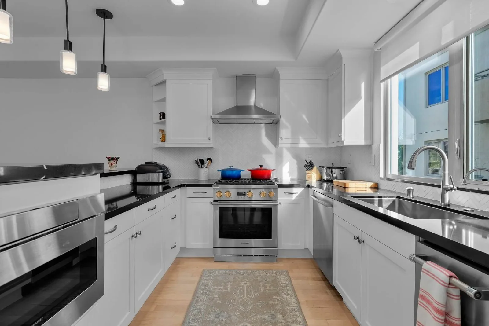 Bright U-shaped kitchen with black countertops, pendant lights and maple floor