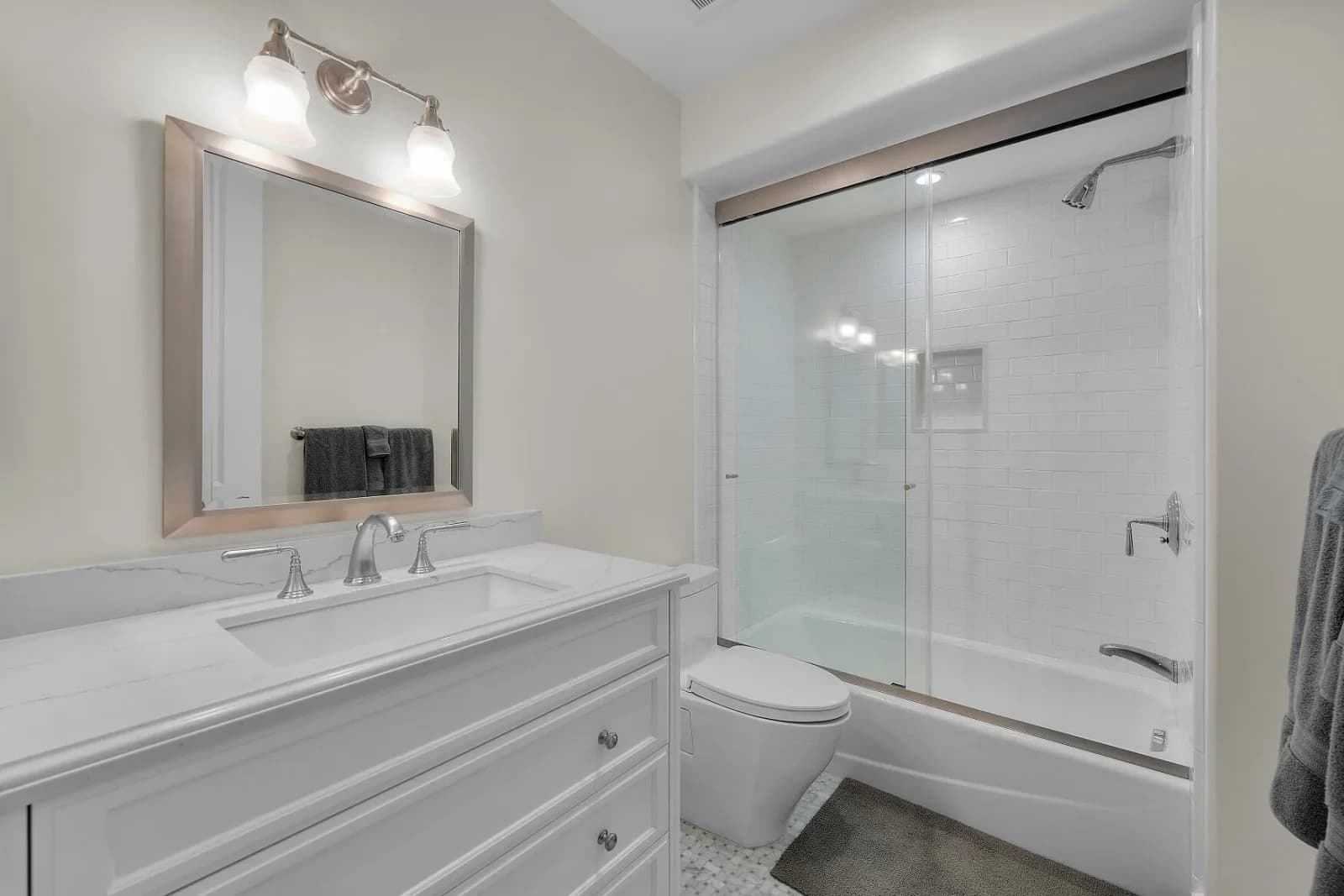 Bathroom with quartz vanity, framed mirror and subway-tiled tub-shower enclosure