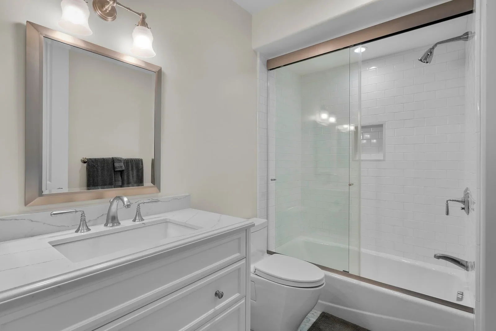Guest bathroom with quartz-top vanity, framed mirror and tiled tub-shower