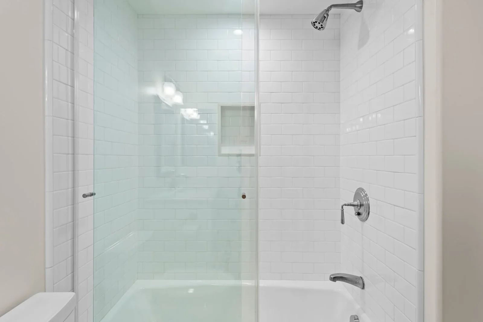 Subway-tiled tub-shower combo with glass sliding door and recessed niche
