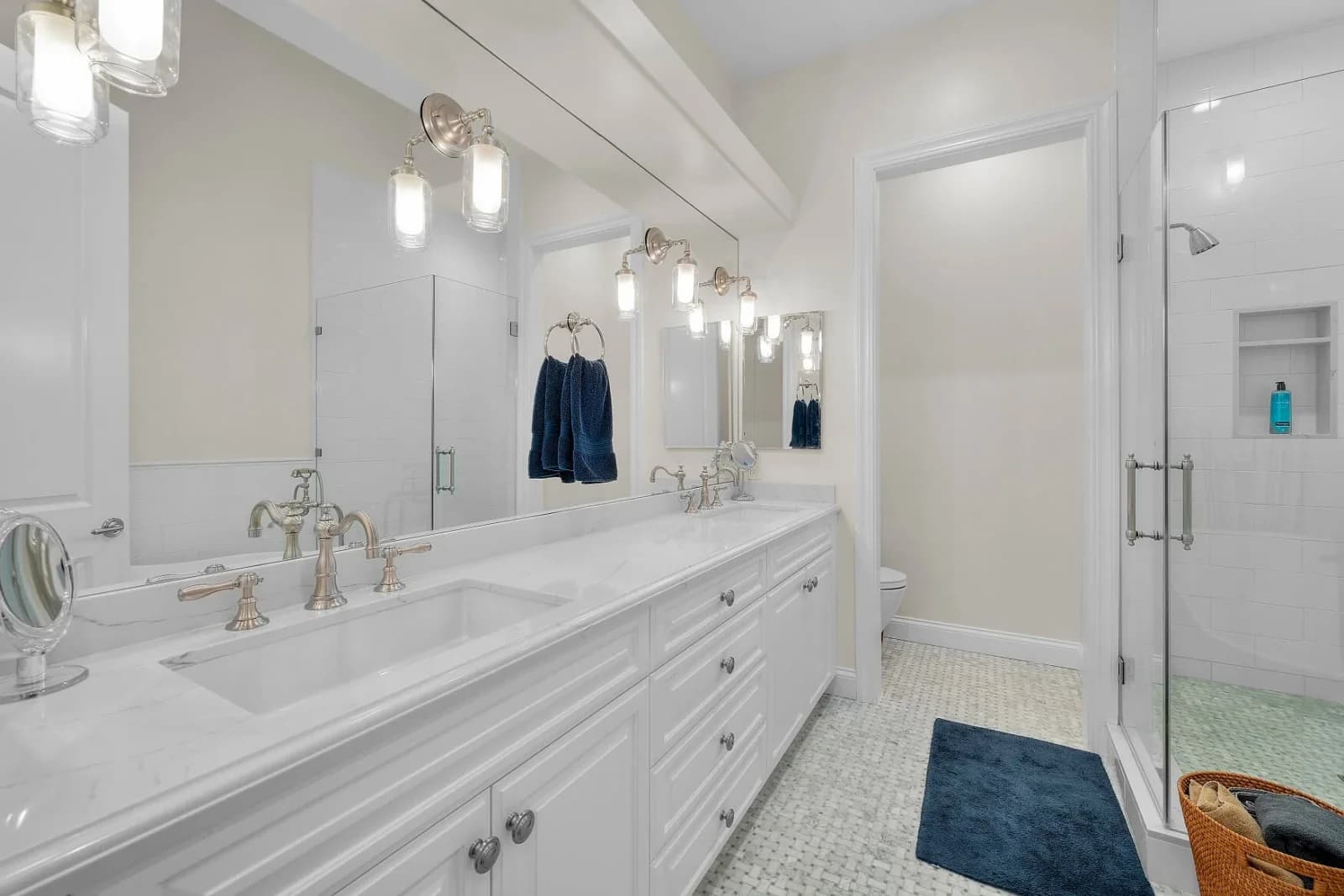Primary bath with white vanity, marble basketweave floor and glass corner shower