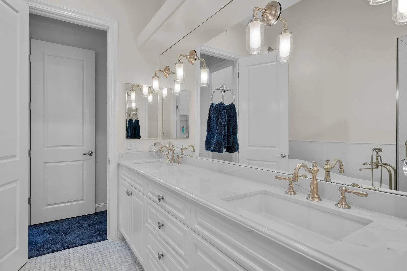 Double marble-top vanity with brushed-gold faucets and glass sconce lighting