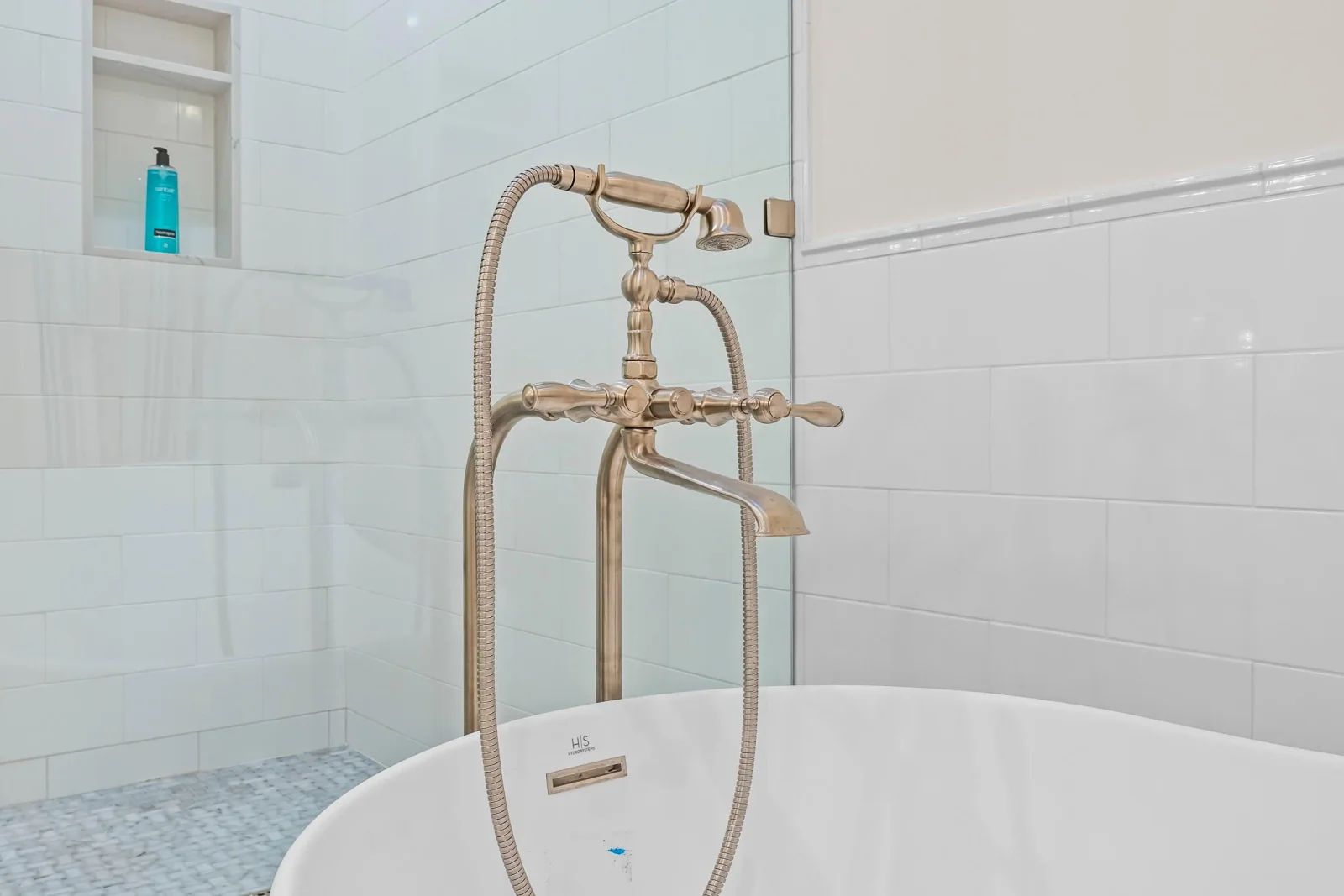 Brushed-nickel vintage tub filler against white subway-tiled bathroom wall