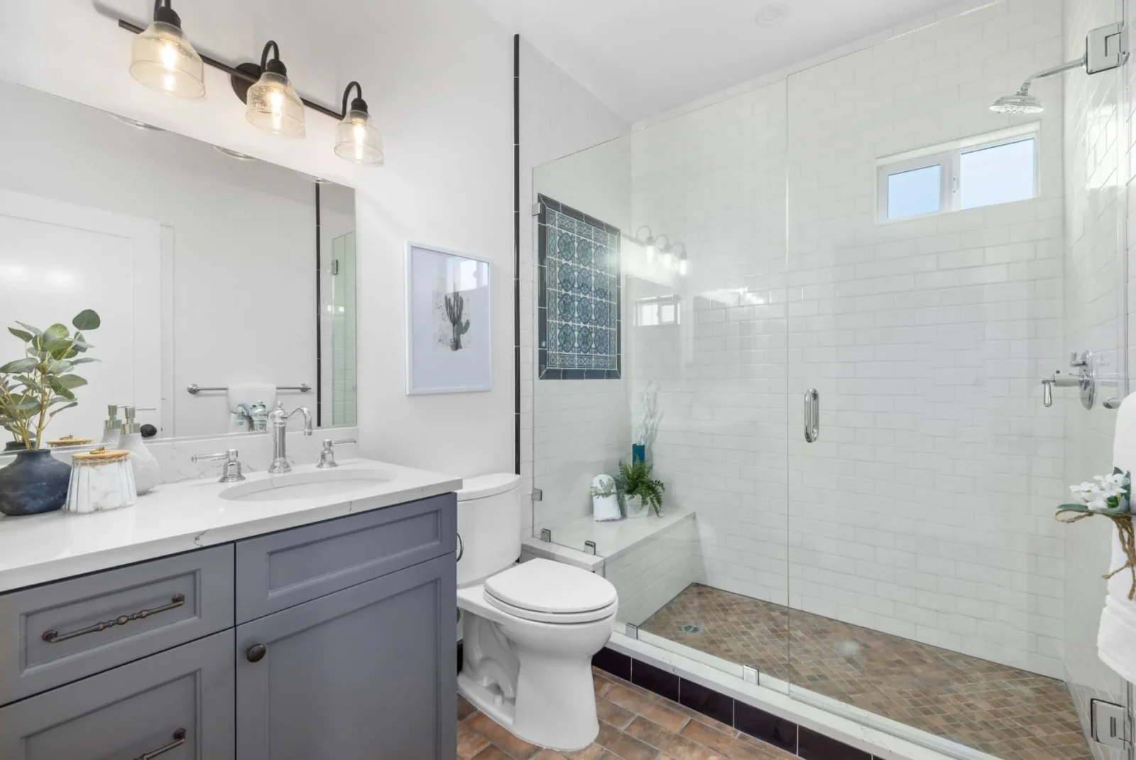 Remodeled bathroom with subway-tile walk-in glass shower, gray vanity, and decorative tile niche