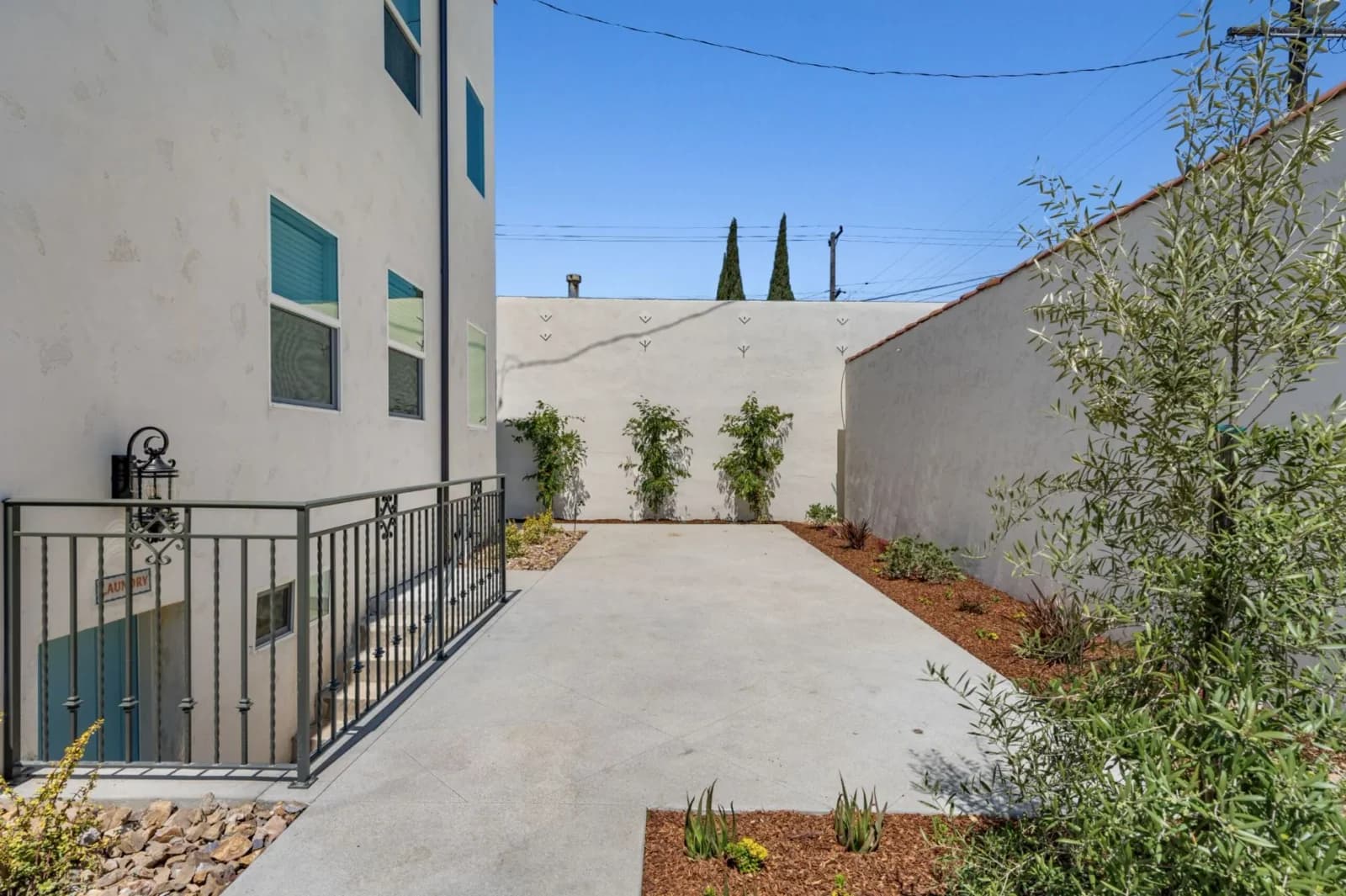 Landscaped concrete side courtyard with new plantings, privacy walls, and iron railing