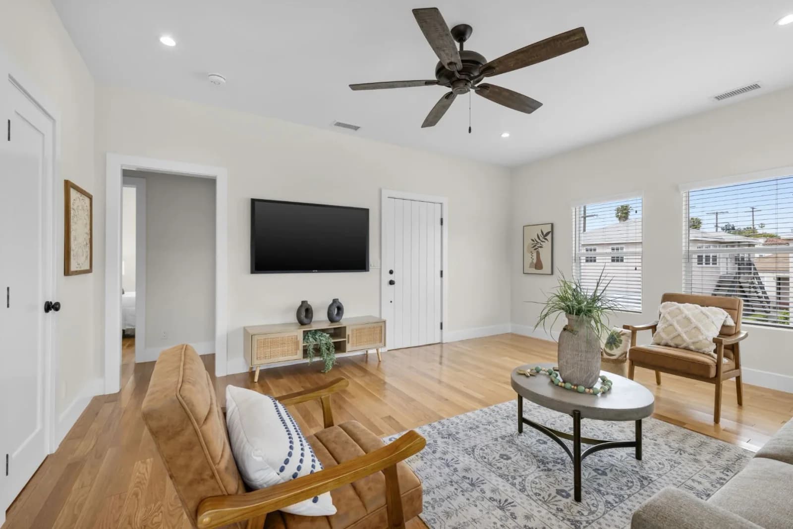 Staged living room with mounted TV, ceiling fan, and hardwood floors near the entry