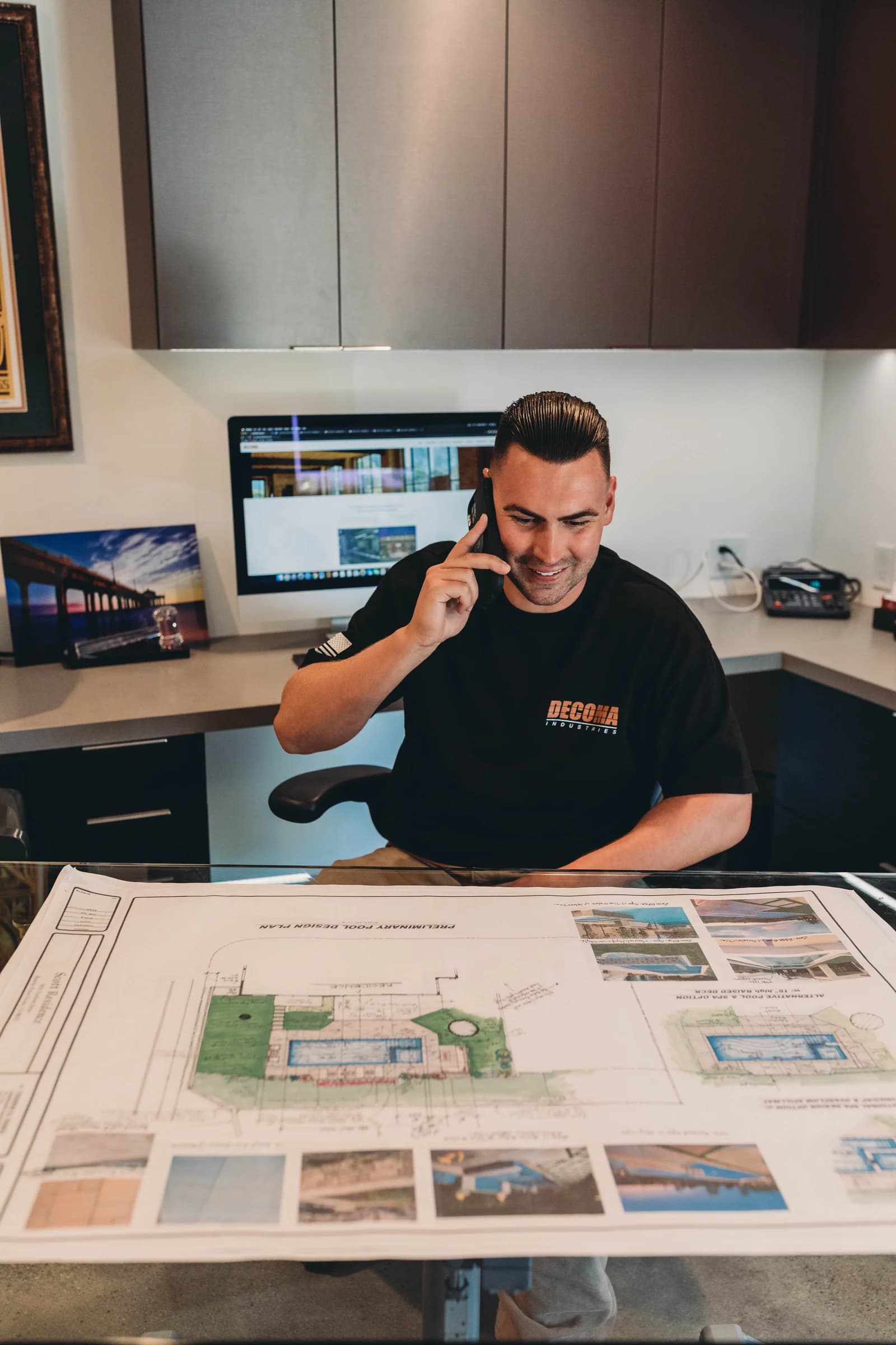 DECOMA Industries project manager taking a client call and reviewing a preliminary pool design plan at the South Bay office