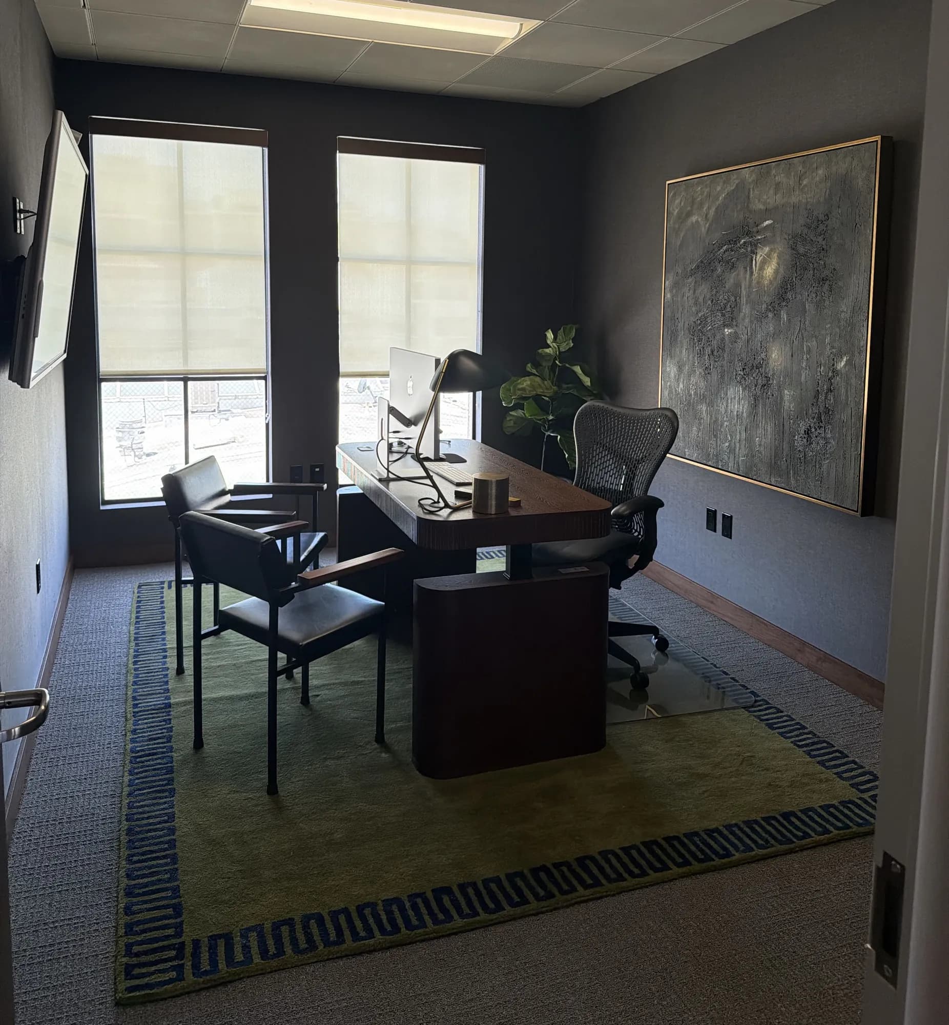 Private executive office with dark walls, a walnut desk, and a patterned rug