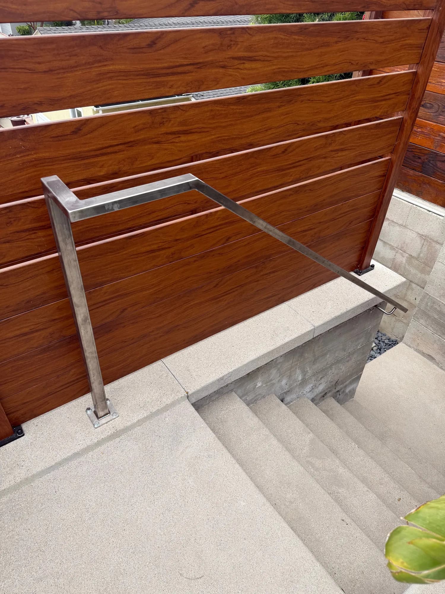 Custom stainless steel handrail on new concrete steps beside a wood privacy screen