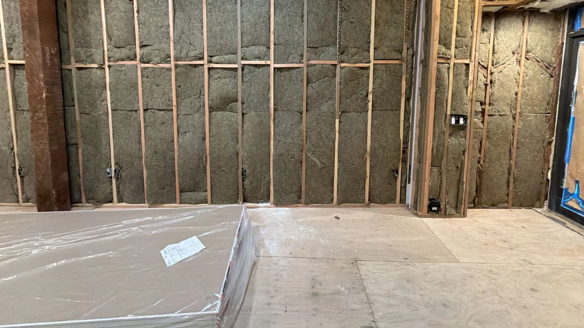 Framed walls packed with mineral-wool insulation and drywall stacked for hanging
