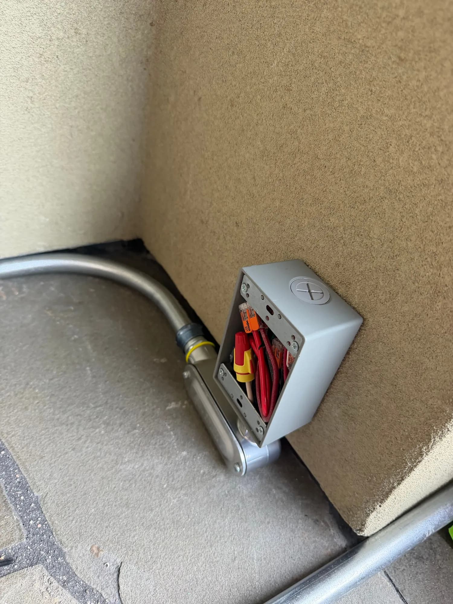 Metal conduit bent to follow the base of the house wall to a junction box by the hot tub